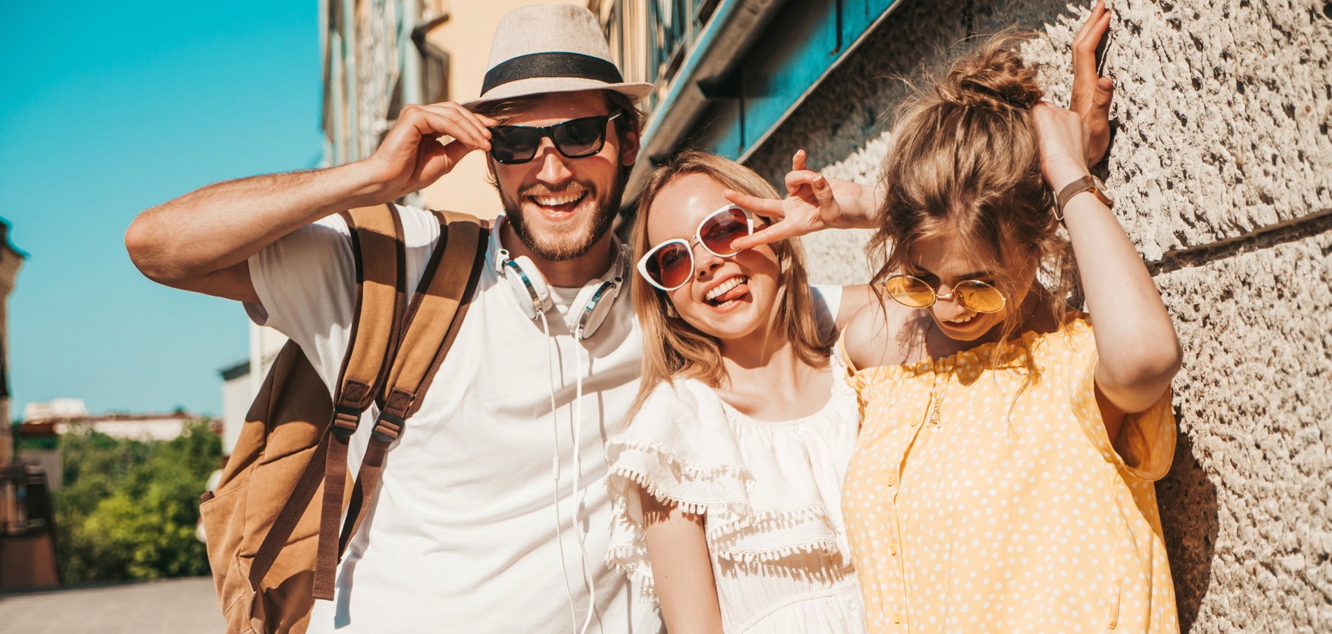 Group of young three stylish friends posing in the street. Fashion man and two cute girls dressed in casual summer clothes. Smiling models having fun in sunglasses.Cheerful women and guy outdoors